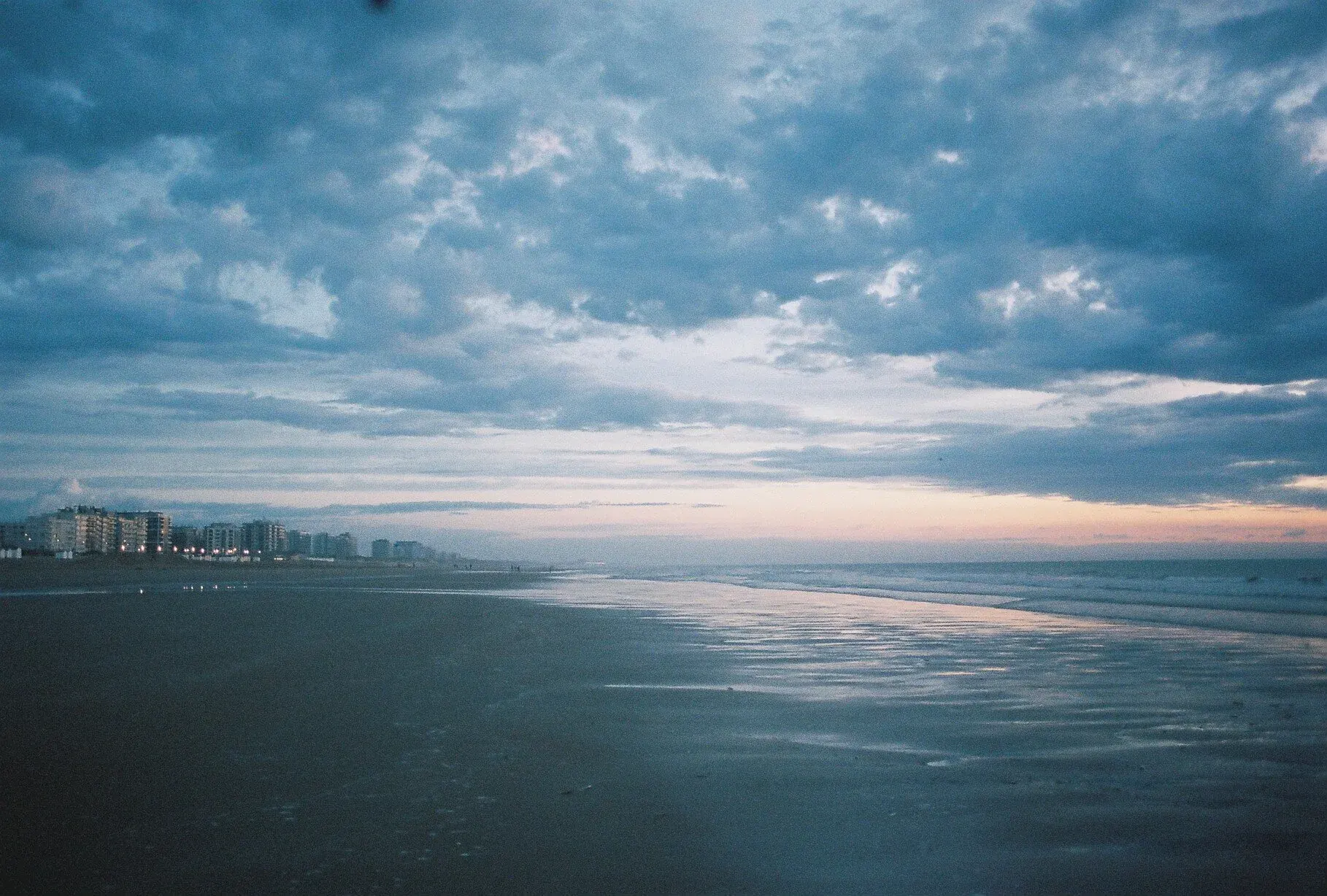 Plage au coucher du soleil avec des bâtiments en arrière-plan et un ciel nuageux.