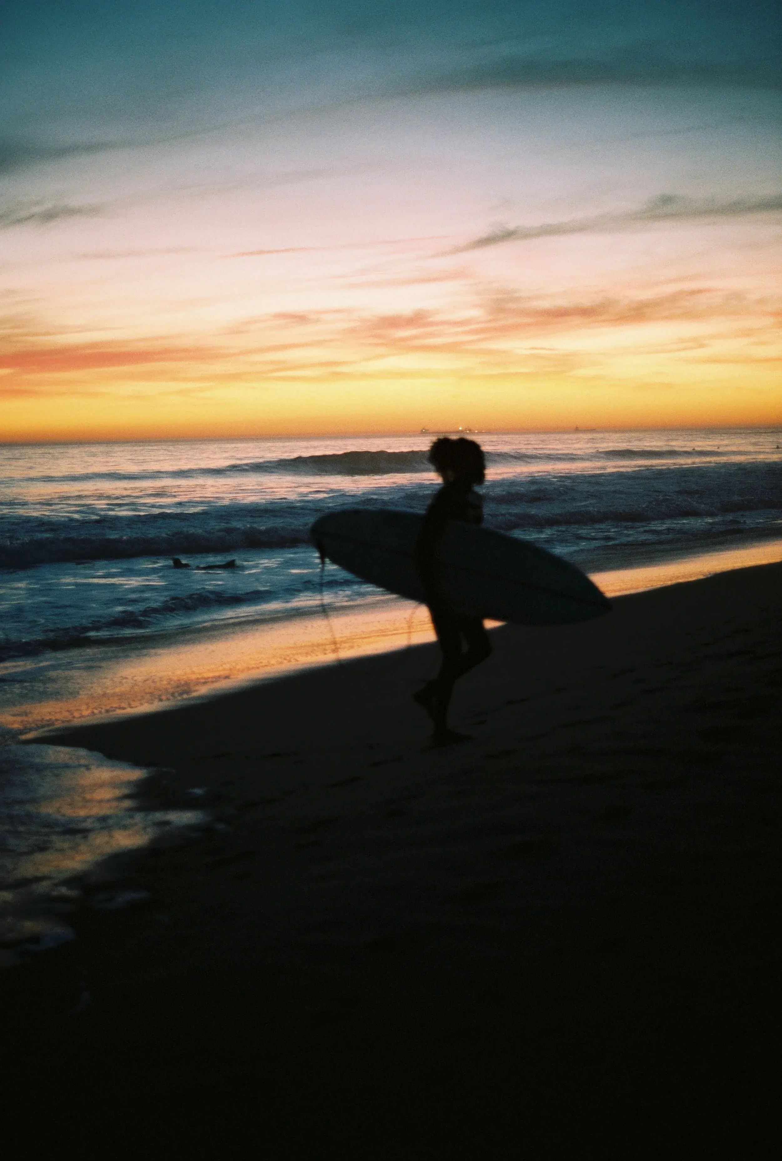 Silhouette d'un surfeur portant une planche de surf sur la plage au coucher de soleil.