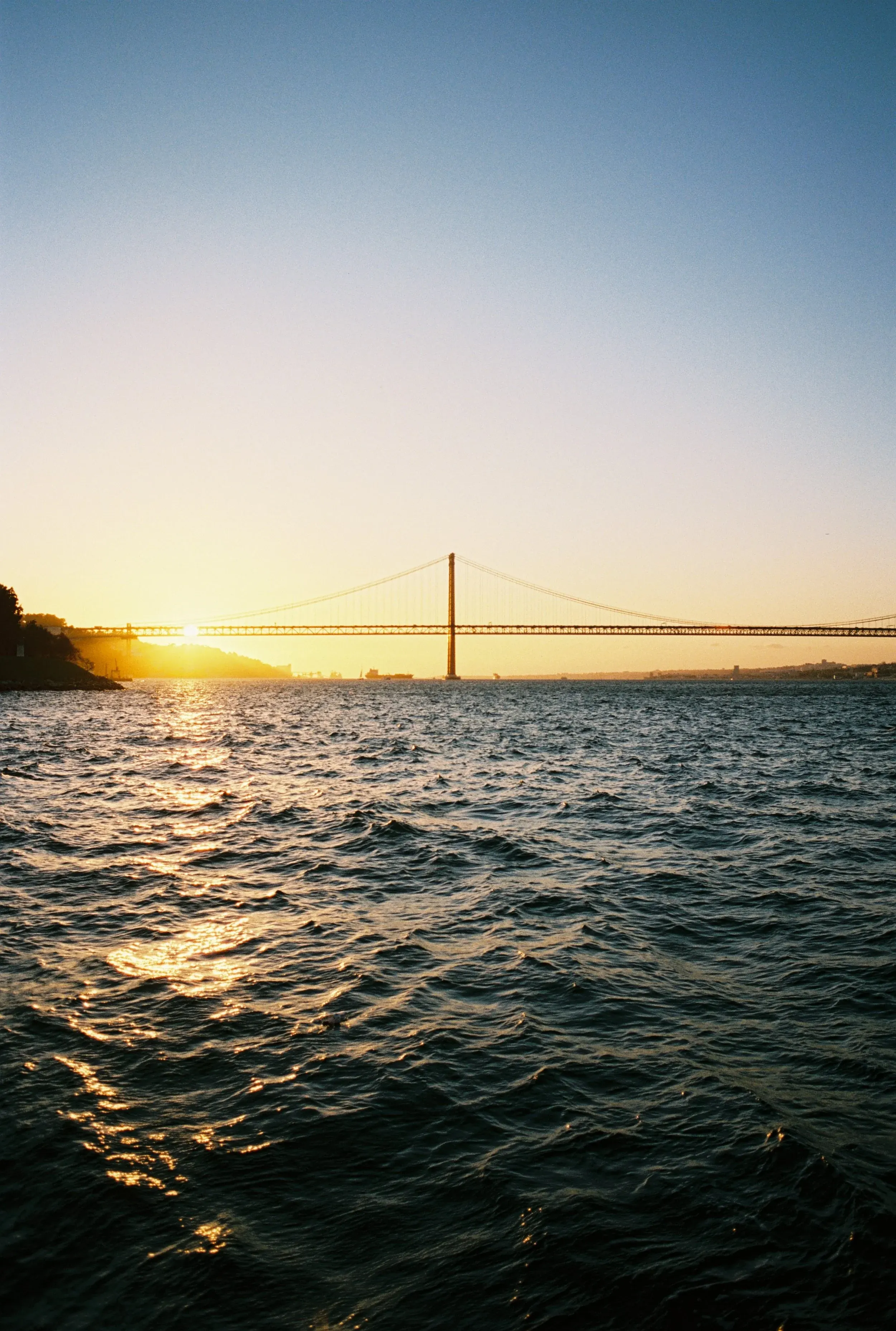 Une vue du pont suspendu au coucher du soleil, avec la mer au premier plan et le ciel clair.