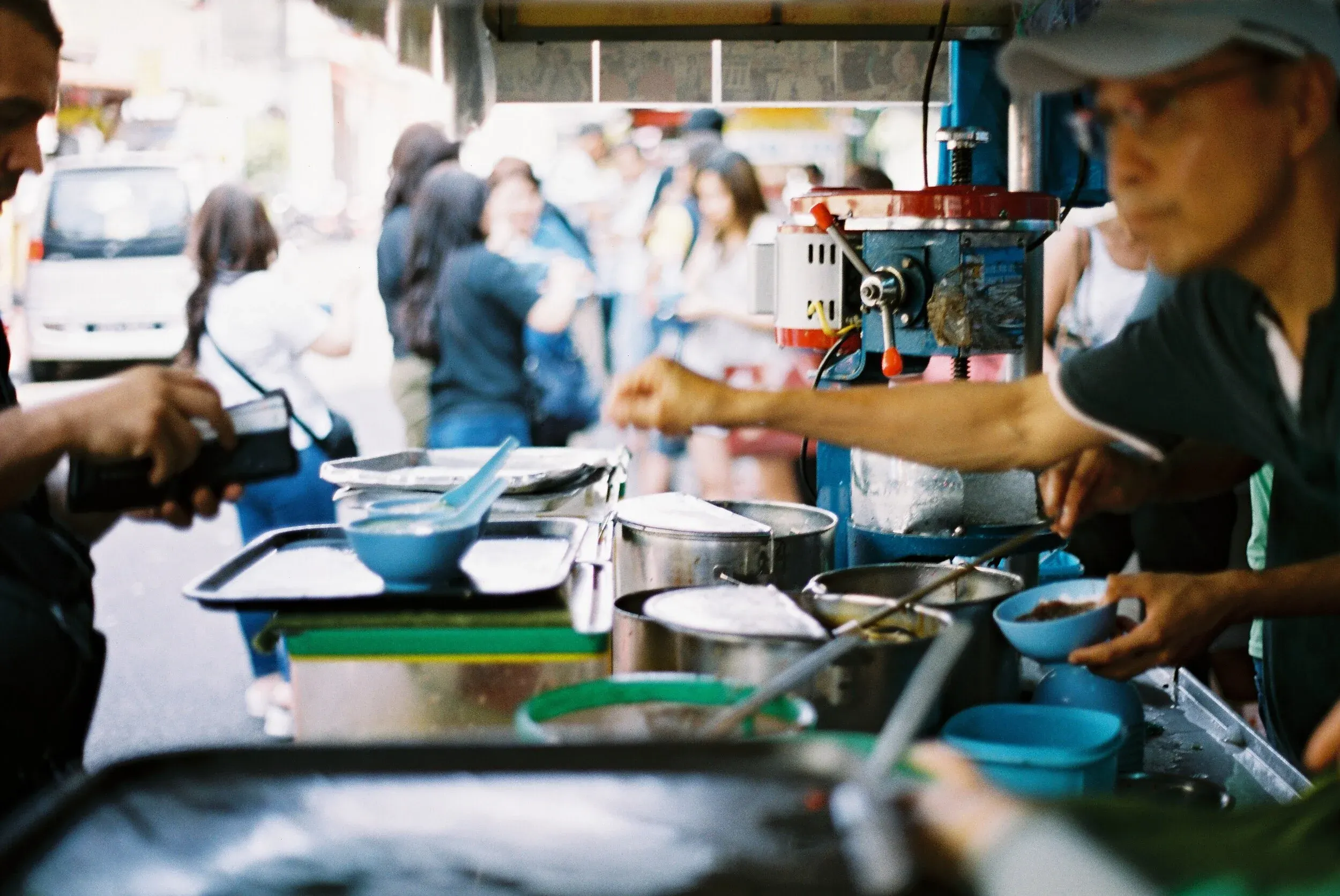 Vendeur de street food servant des plats à un client dans une rue animée avec plusieurs personnes en ligne.