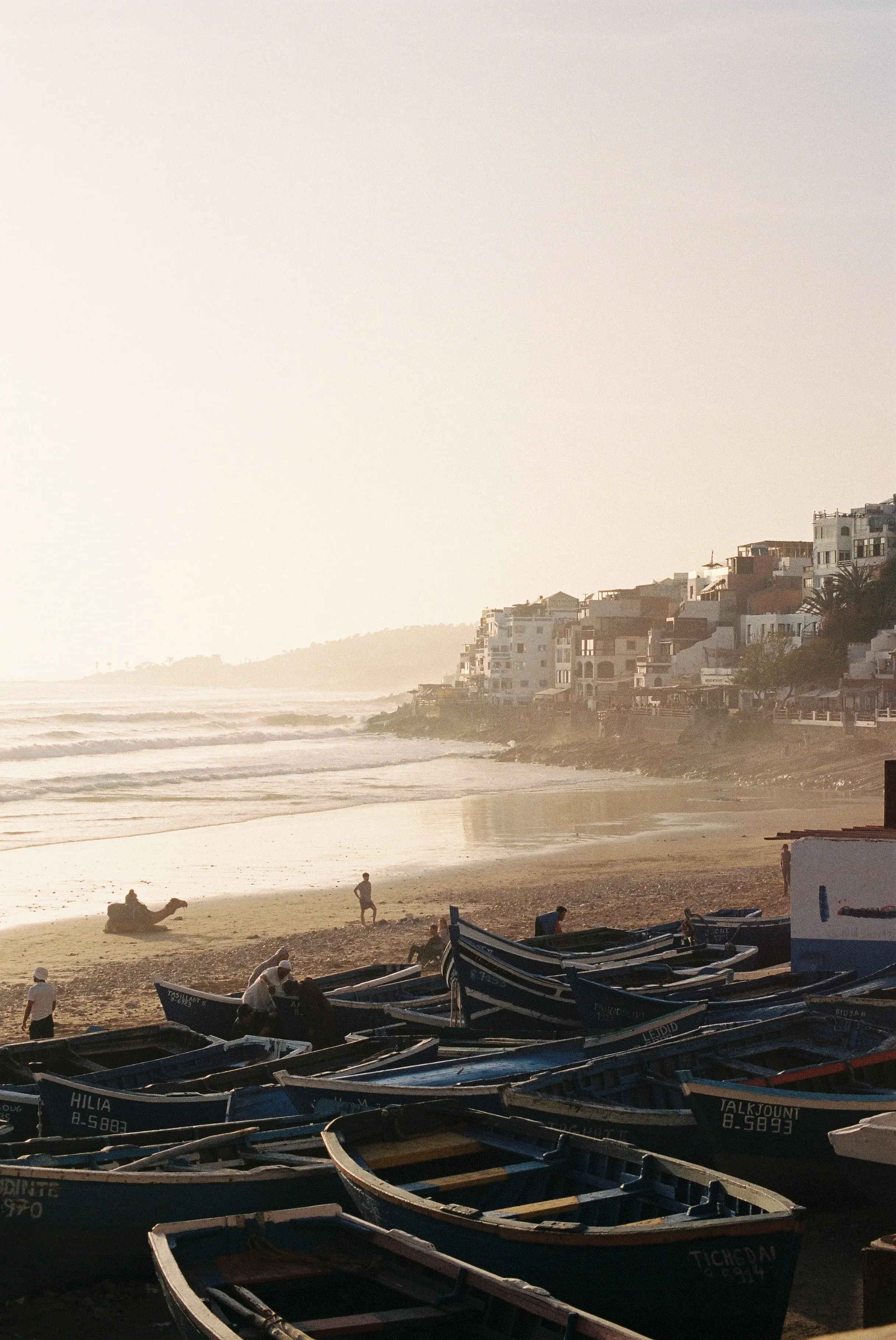 Bateaux en bois sur une plage au coucher du soleil, avec des bâtiments en colline en arrière-plan.