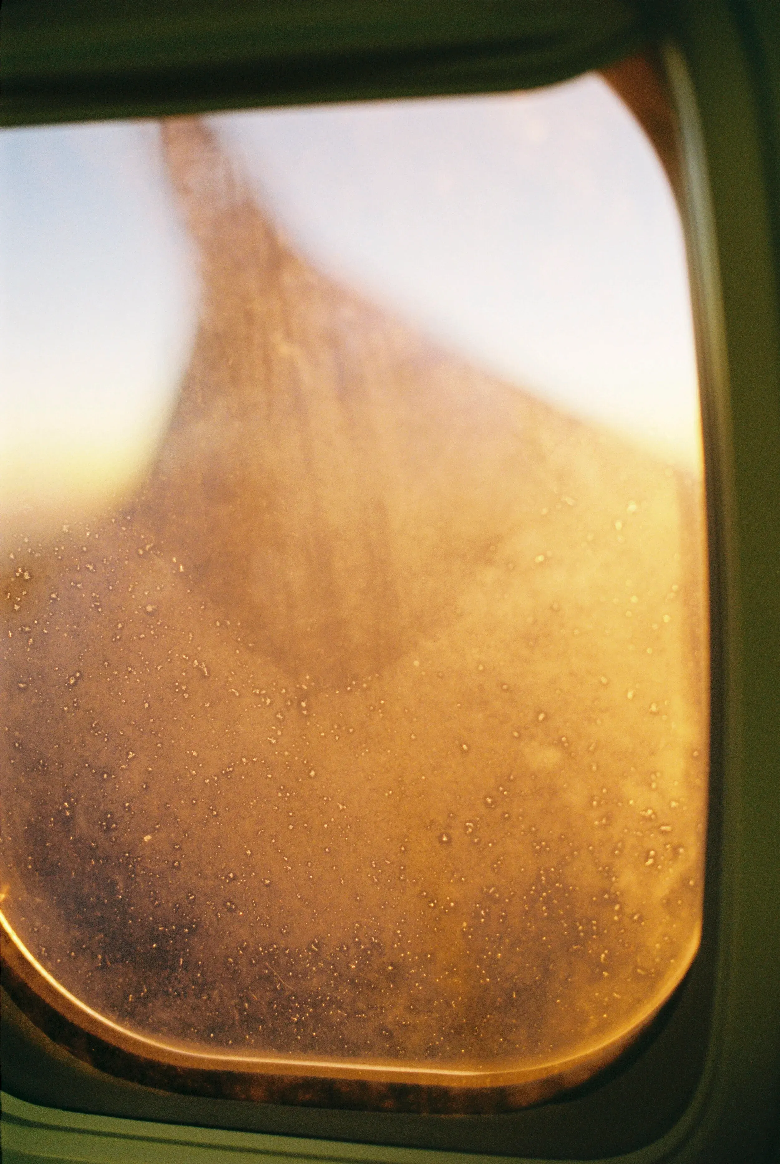Vue à travers une fenêtre d'avion sale, avec des gouttes d'eau et une vue floue de la silhouette d'une montagne ou d'un immeuble en arrière-plan.