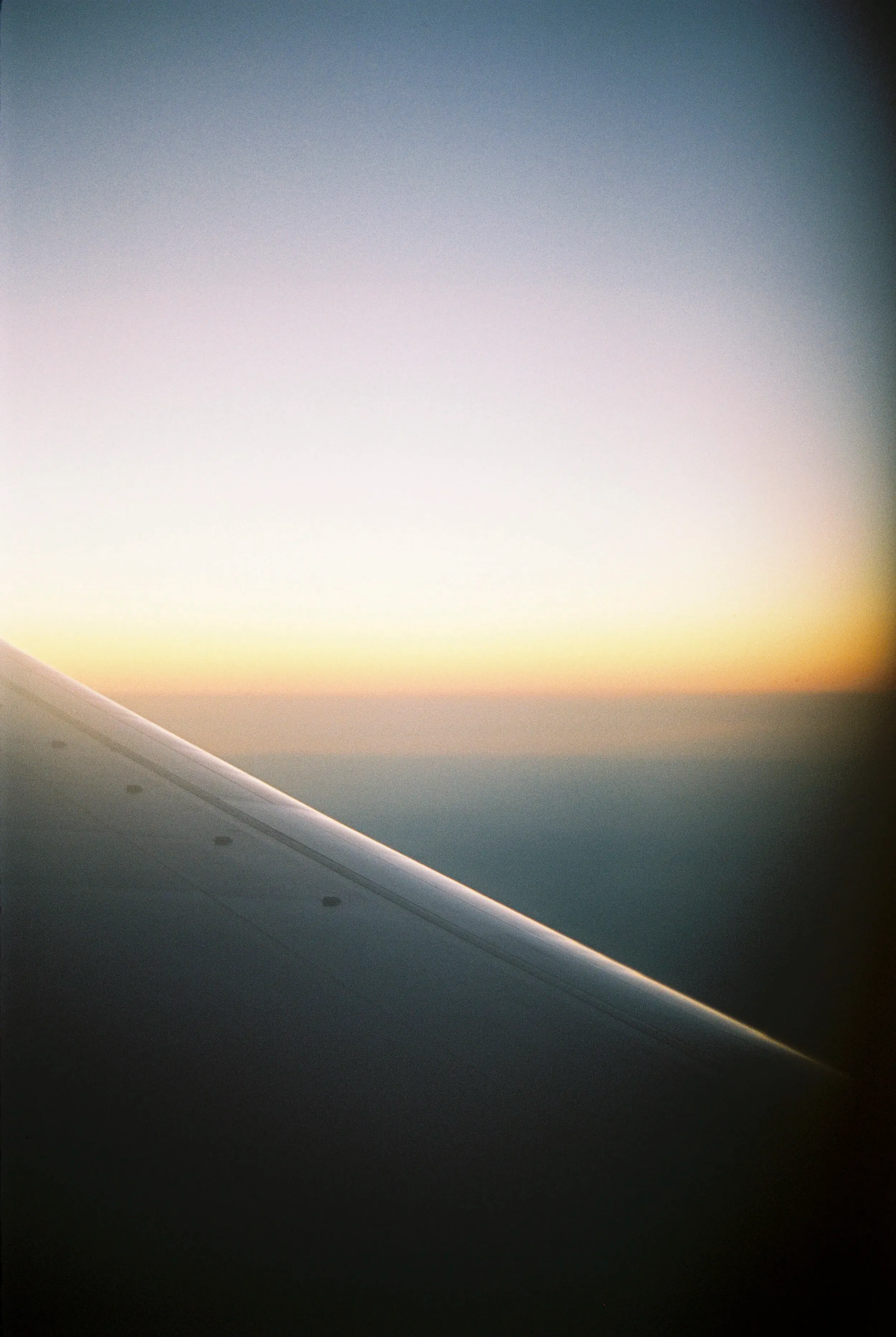 Vue depuis un avion montrant l'aile en premier plan et un ciel coloré au coucher du soleil.