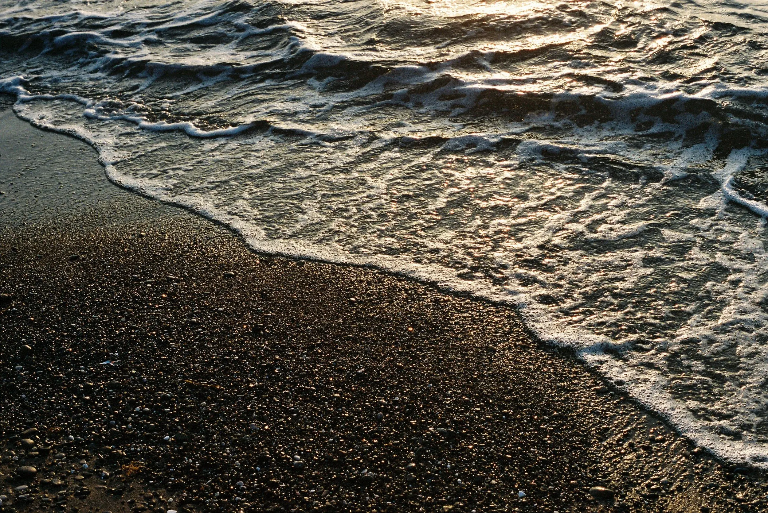Vague de mer lavée sur le sable noir de la plage au coucher du soleil.
