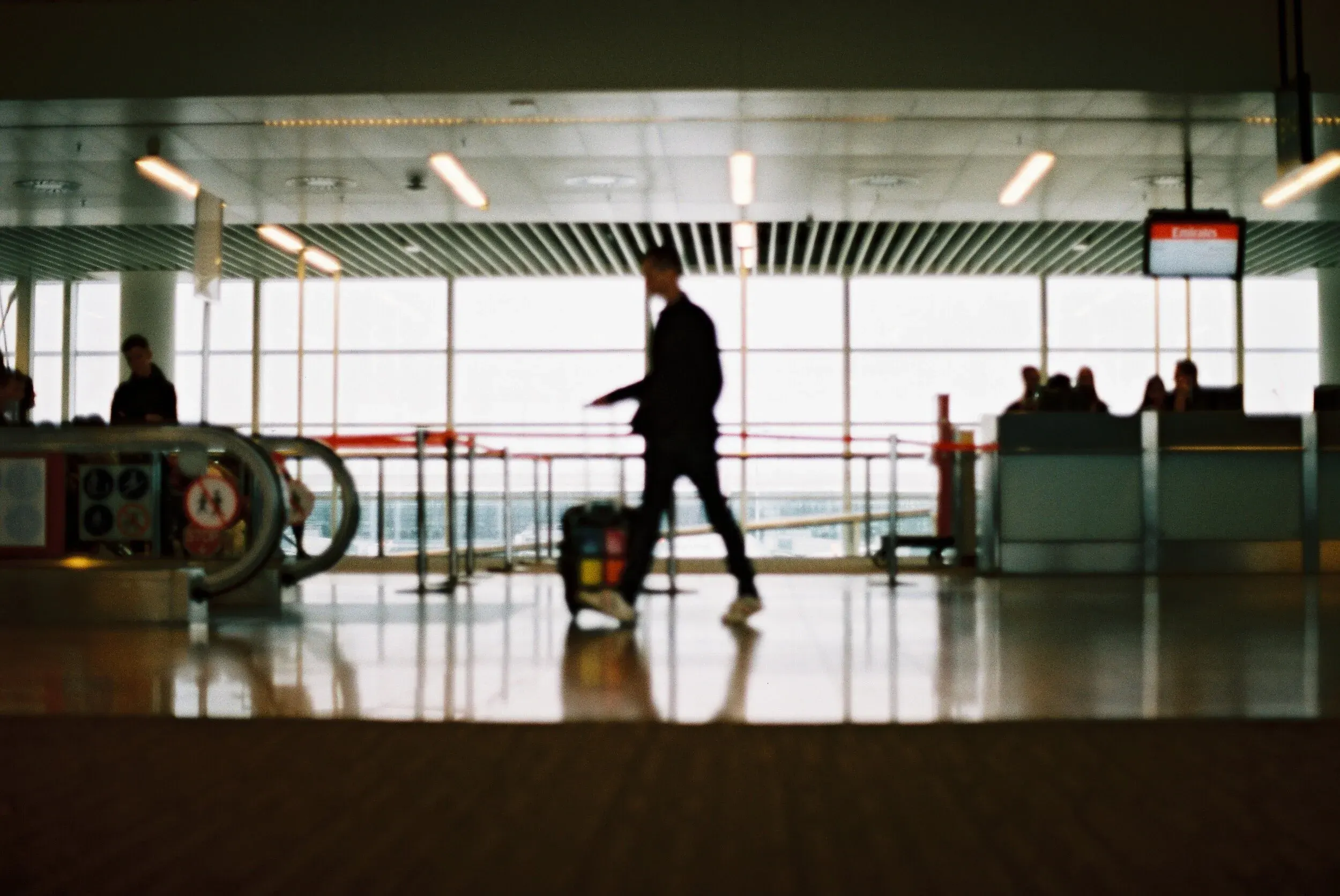 Personne avec une valise marchant dans un aéroport en arrière-plan, fenêtres et autres passagers assis.