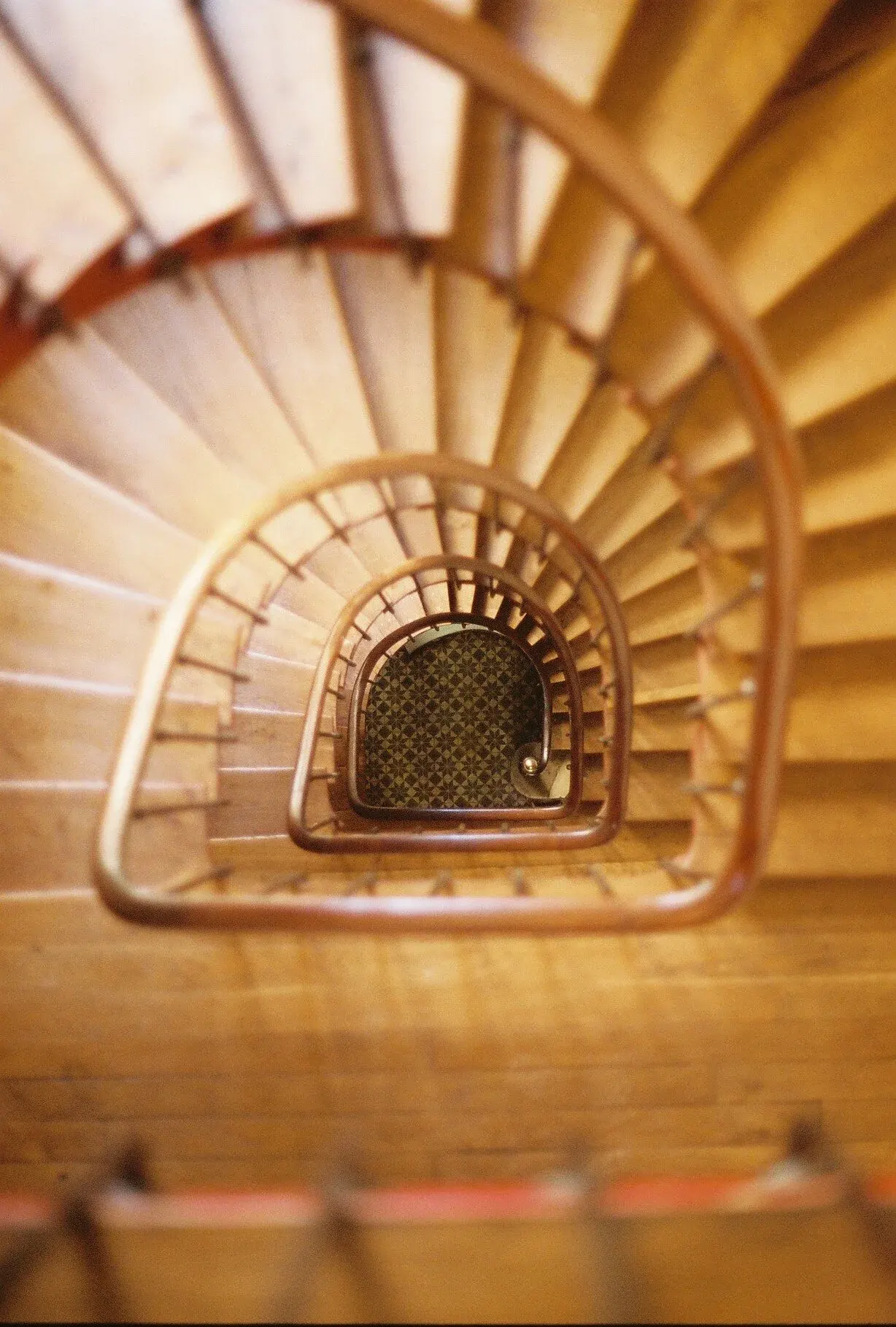 Vue du haut d'une cage d'escalier en spirale en bois, regardant vers le bas, avec un sol à motifs en mosaïque.