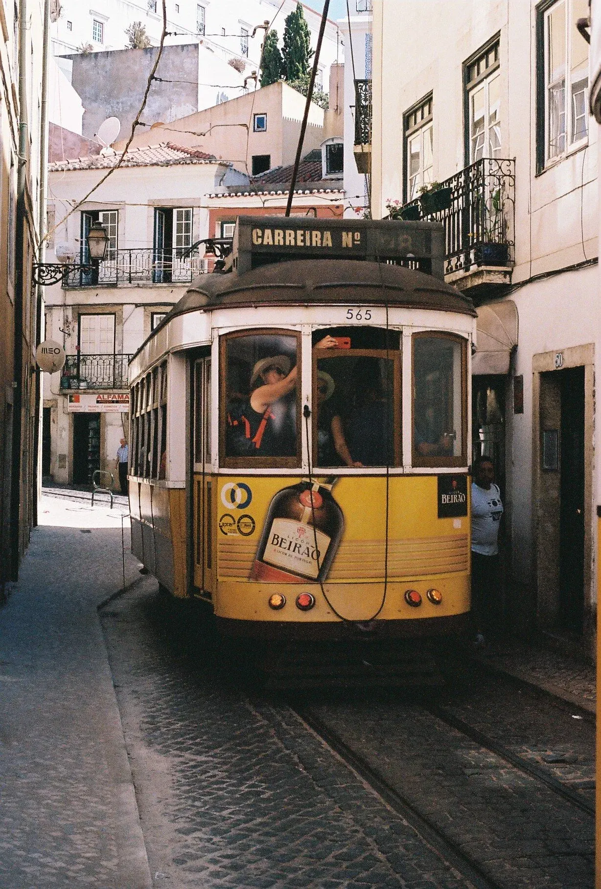 Un tramway jaune en mouvement dans une rue urbaine avec des bâtiments colorés, passant devant des immeubles avec balcons en fer forgé.