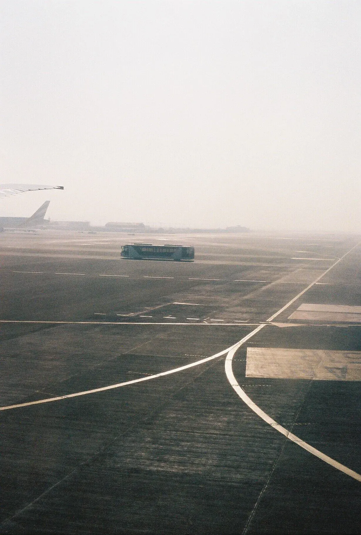 Vue d'un tarmac d'aéroport sous un ciel brumeux, avec un bus au centre et des avions en arrière-plan, dont un avec un ginormous aileron.