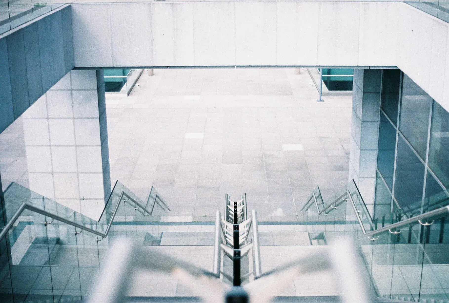 Vue vers un escalier en verre menant à une grande cour intérieure d'un bâtiment moderne en béton et verre