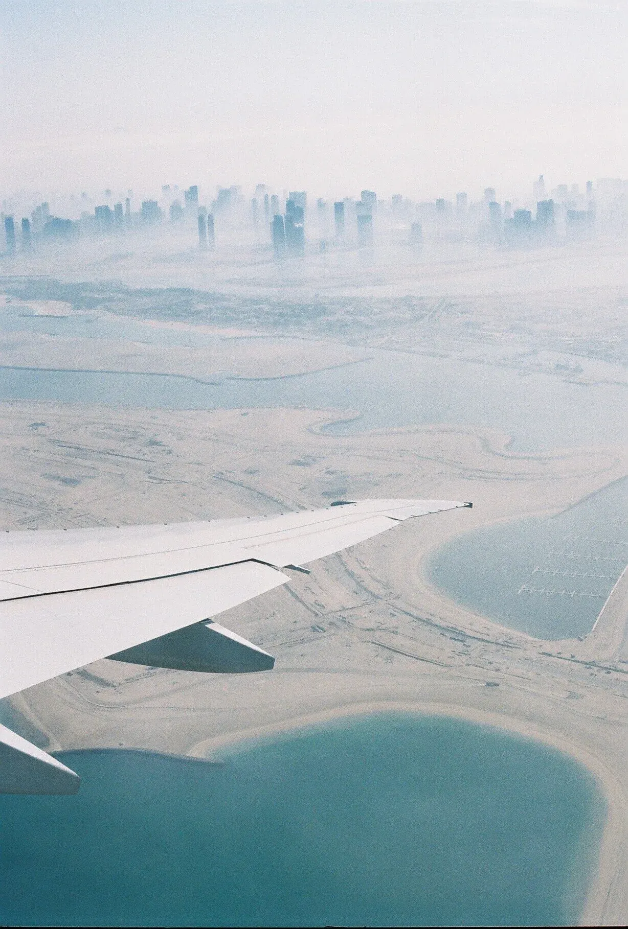 Vue aérienne d'une grande ville avec de nombreux gratte-ciel à l'horizon, des plans d'eau et un paysage désertique, pris depuis un avion en vol.