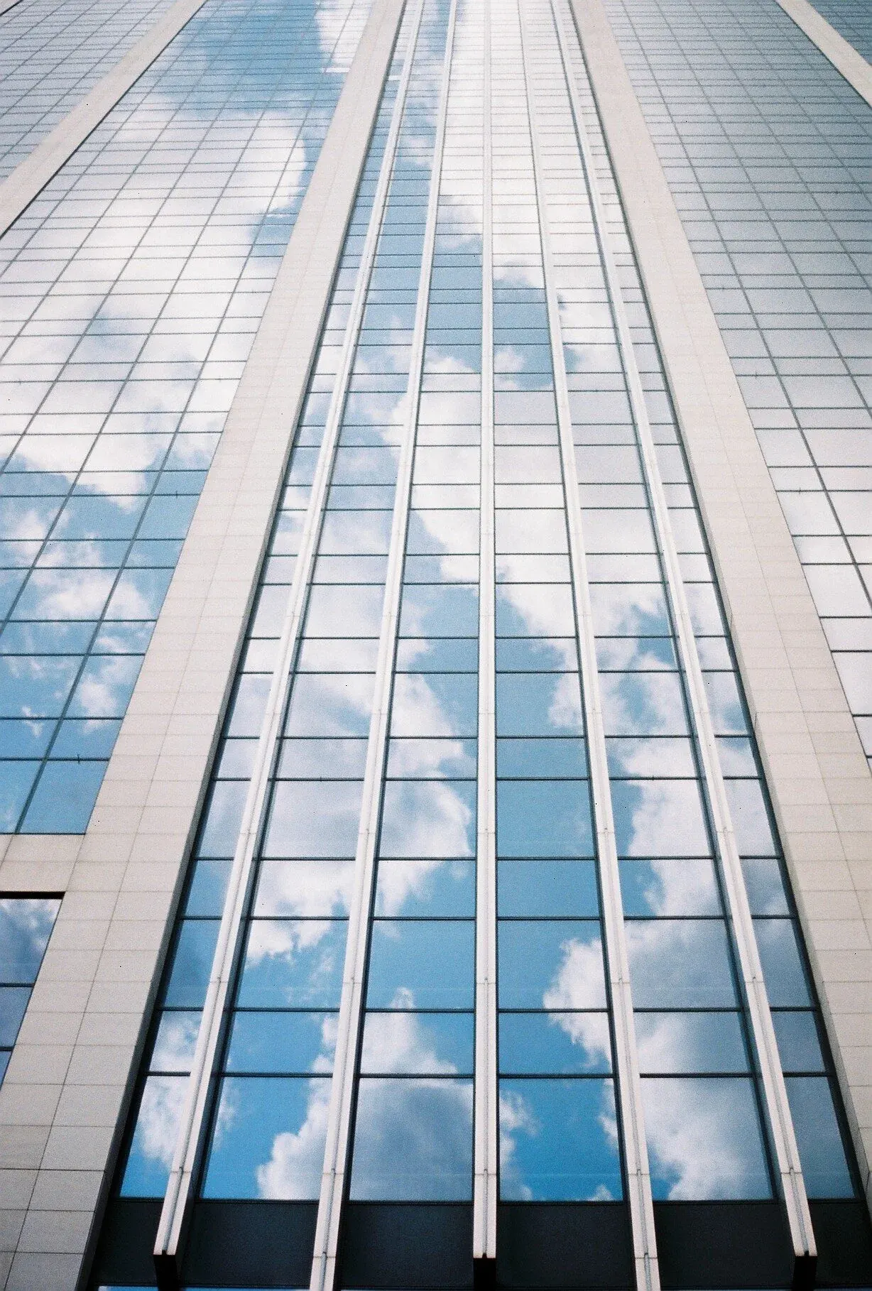 Gratte-ciel moderne avec façade en verre reflétant le ciel et les nuages.