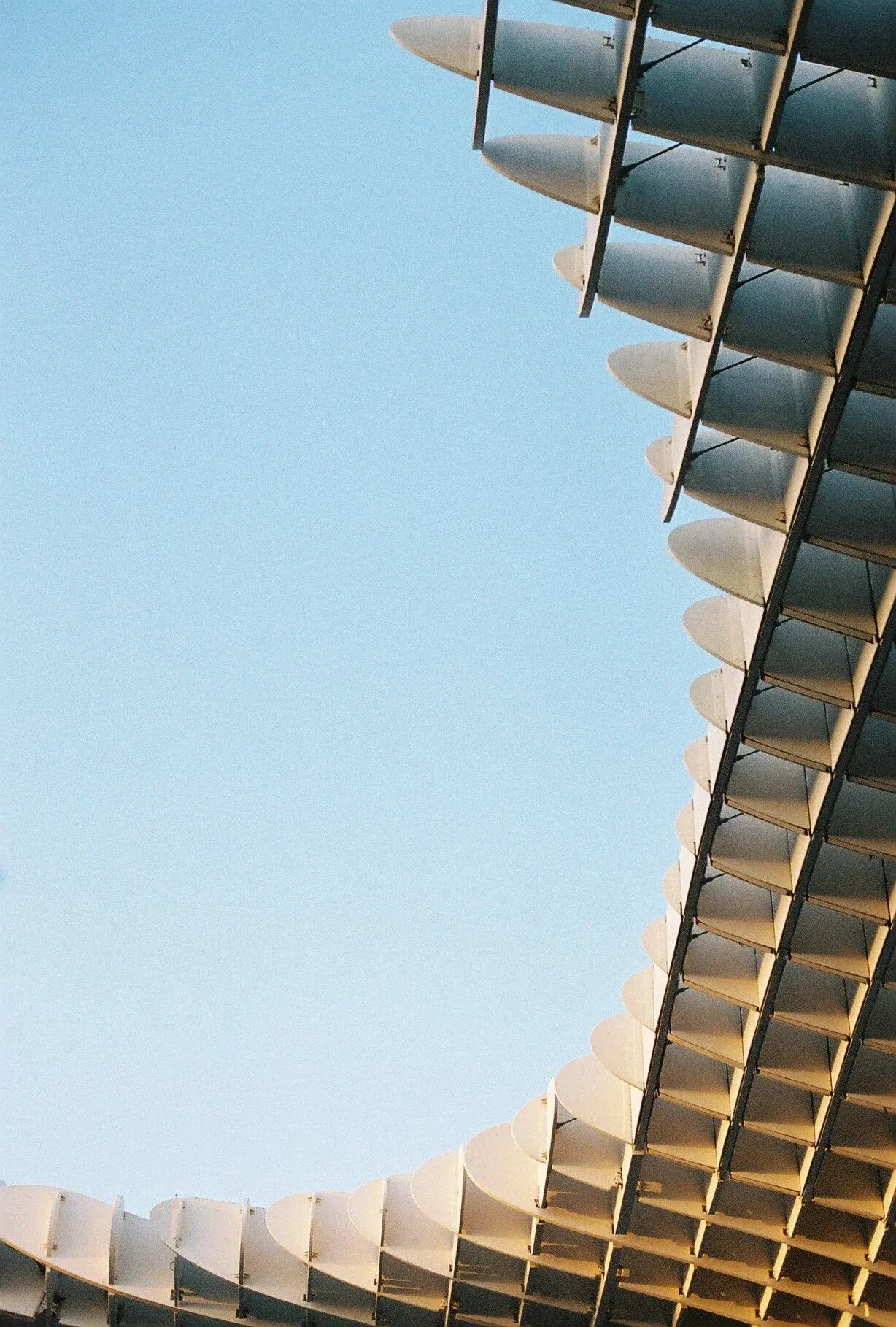 Vue d'une structure architecturale moderne avec des façades en forme de vagues et des panneaux solaires, contre un ciel bleu.
