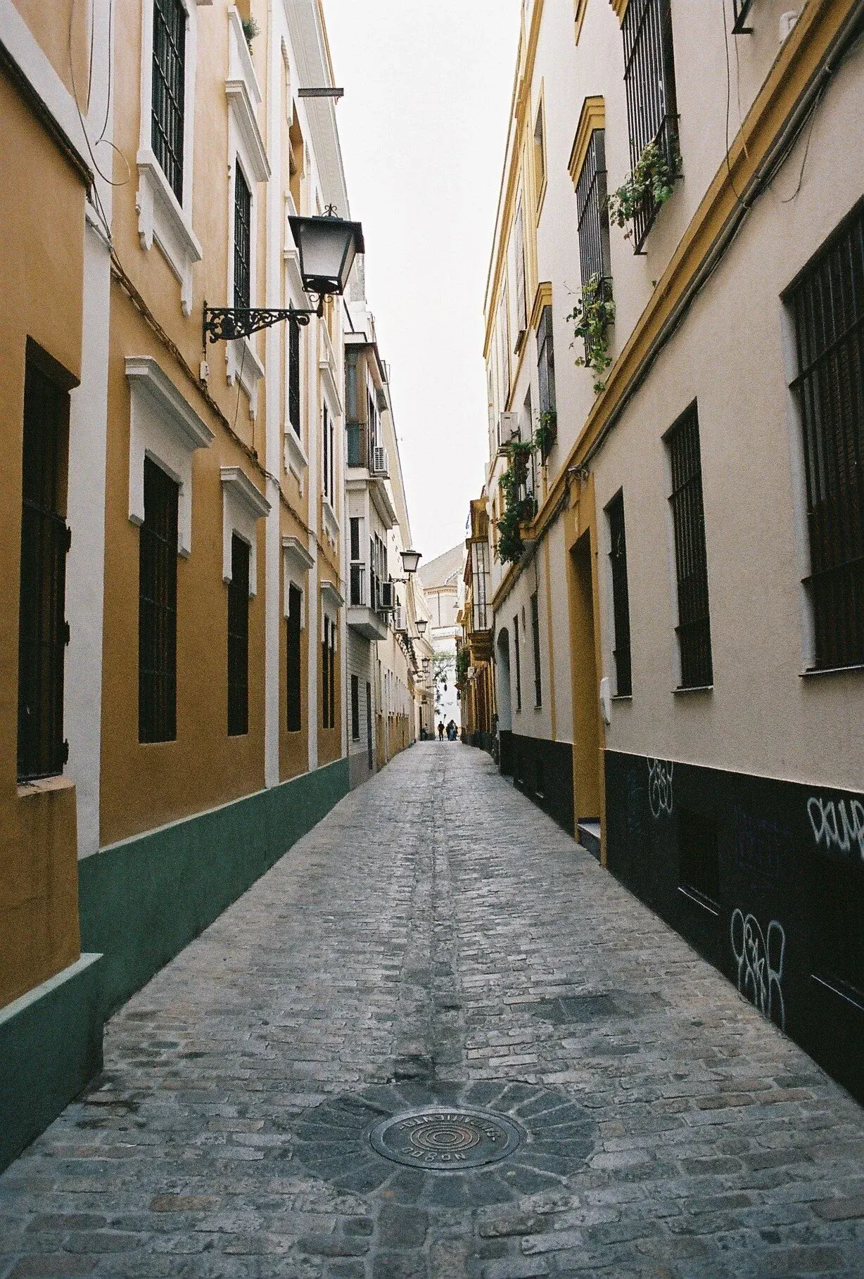 Une ruelle pavée bordée de bâtiments colorés, avec des lampadaires en fer forgé et des fenêtres avec des barreaux.