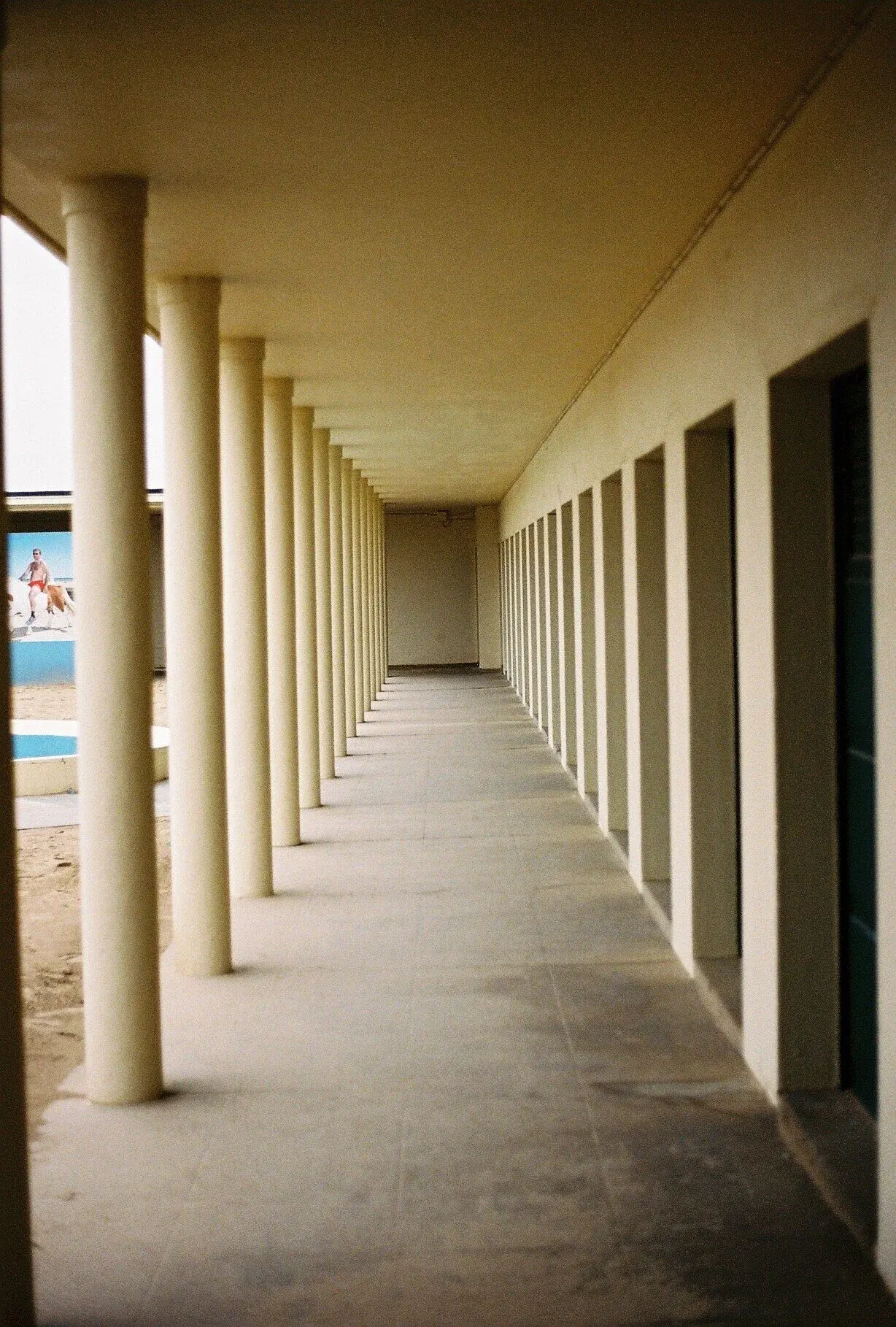 Vue d'un couloir avec des colonnes blanches sur le côté gauche et des fenêtres dans le mur droit.