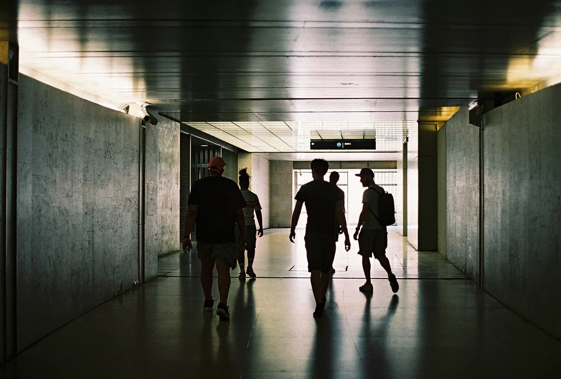 Silhouettes de plusieurs personnes marchant dans un tunnel lumineux à l'extérieur.