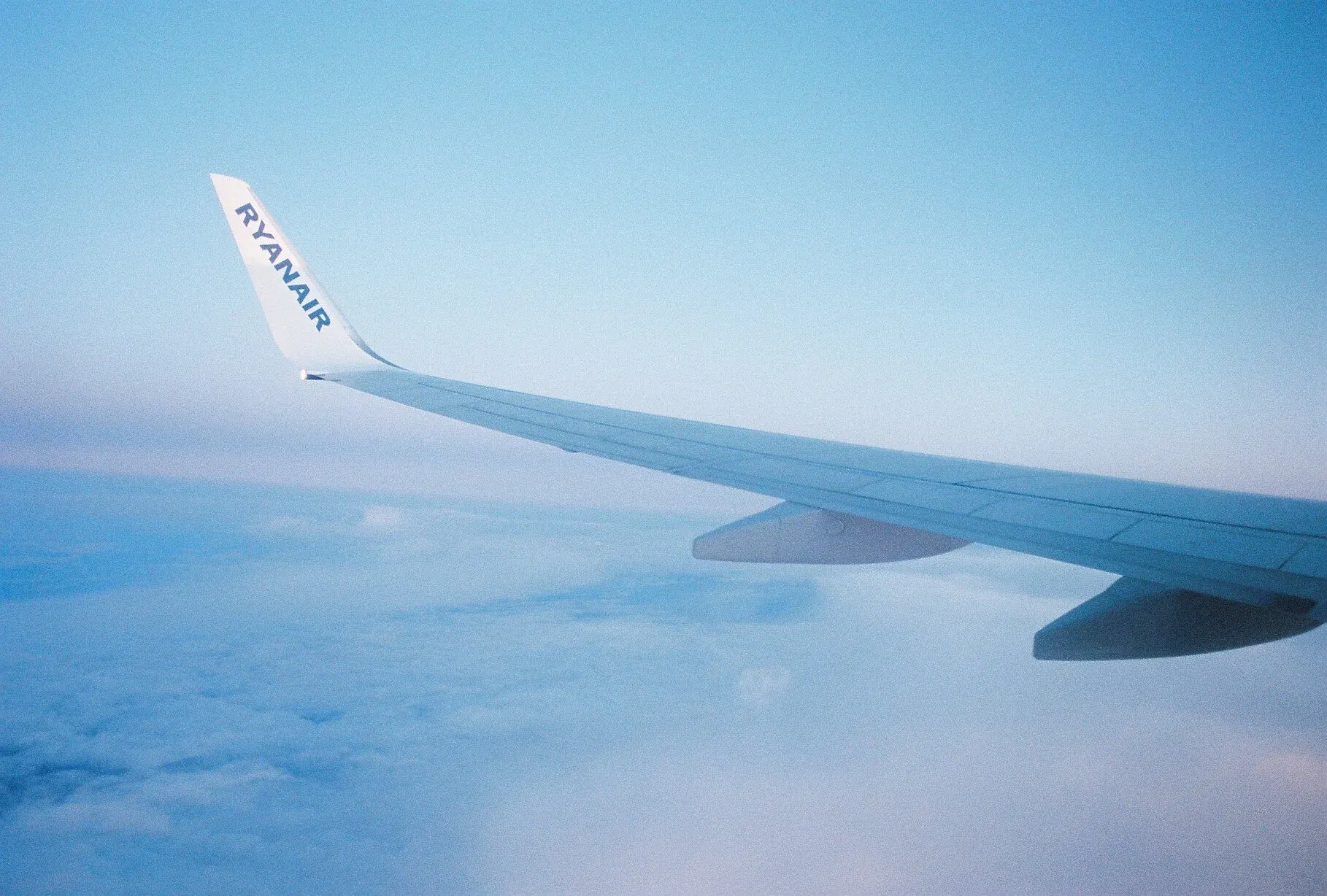 Vue depuis un avion montrant une aile avec le logo 'RYANAIR' au-dessus de nuages et d'un ciel bleu clair.