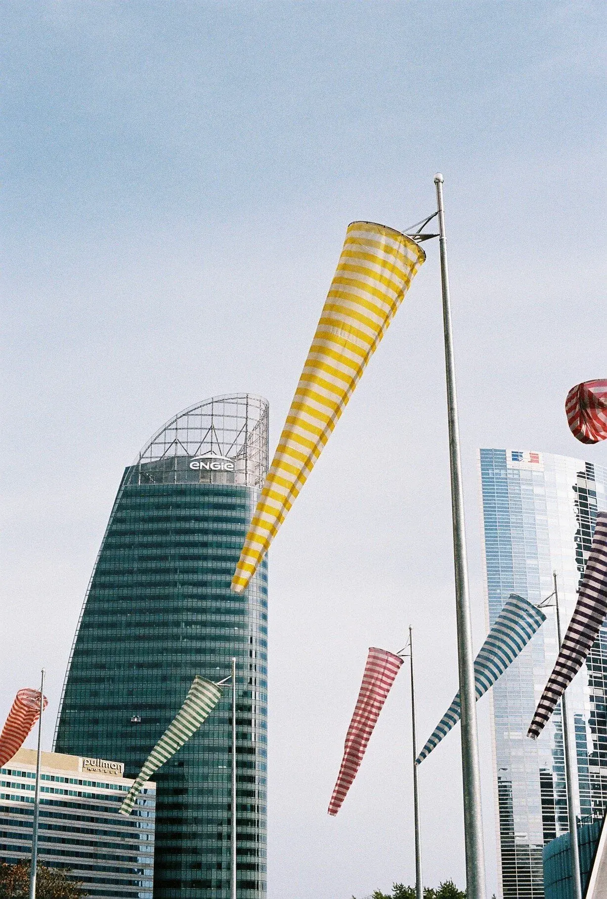 Des drapeaux de plusieurs couleurs et motifs flottent dans le vent devant des gratte-ciel modernes dans une ville.